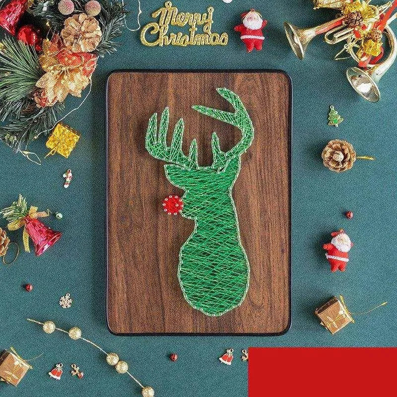 a string art deer on a wooden board surrounded by christmas decorations